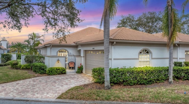 mediterranean / spanish-style home with a garage, a tile roof, a gate, and decorative driveway