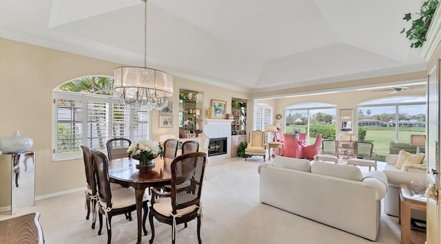 carpeted dining space featuring baseboards, a raised ceiling, a glass covered fireplace, crown molding, and a chandelier