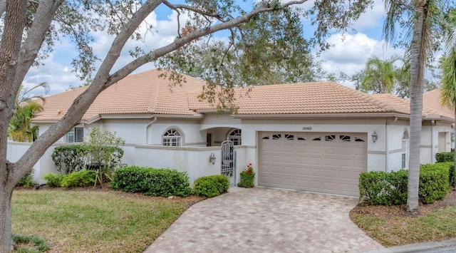 view of front of home featuring a tiled roof, an attached garage, fence, decorative driveway, and stucco siding