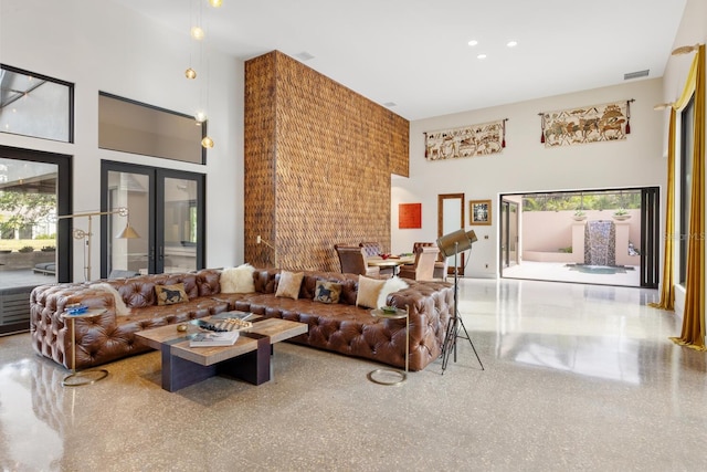 living area with a towering ceiling, visible vents, french doors, and speckled floor