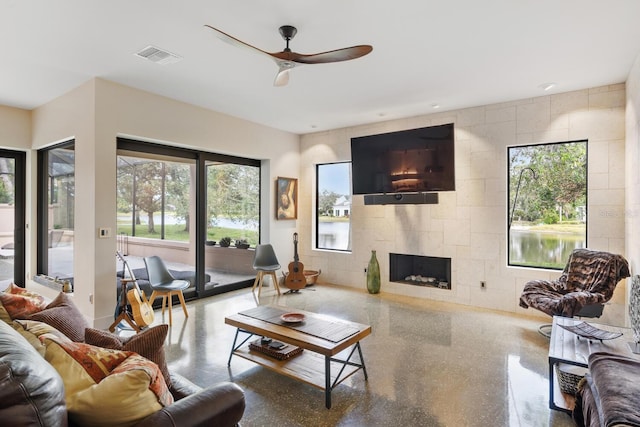 living room featuring a tile fireplace, visible vents, ceiling fan, and speckled floor