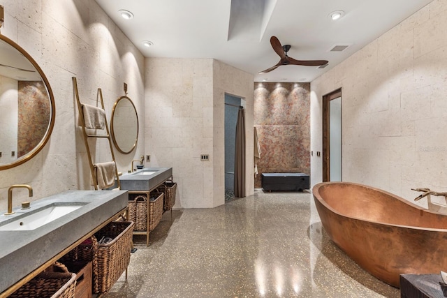 bathroom with concrete block wall, two vanities, a sink, and a freestanding bath