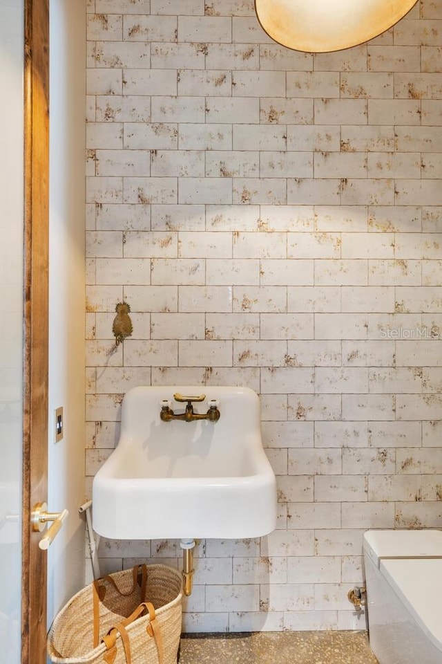 half bath with brick wall, a sink, and toilet