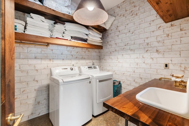 washroom featuring brick wall, laundry area, a sink, and washer and dryer