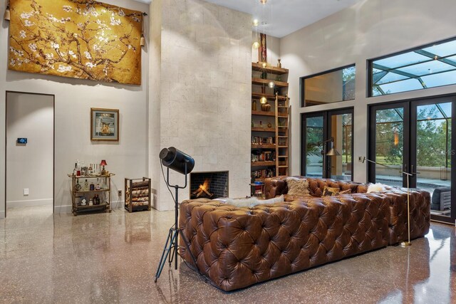 living room with a tile fireplace, speckled floor, a towering ceiling, baseboards, and french doors