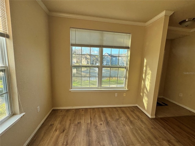 empty room featuring crown molding, baseboards, and wood finished floors