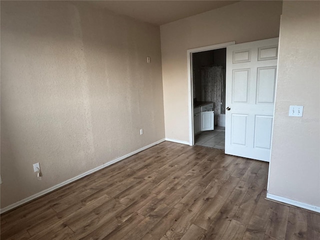 unfurnished bedroom with dark wood-style floors, ensuite bath, and baseboards