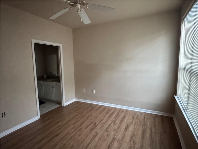 unfurnished bedroom with ensuite bathroom, wood finished floors, a ceiling fan, and baseboards