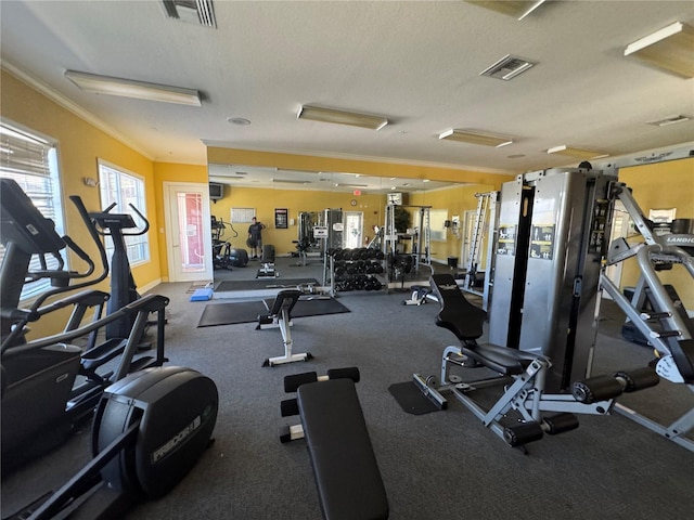 exercise room with ornamental molding, visible vents, and a textured ceiling