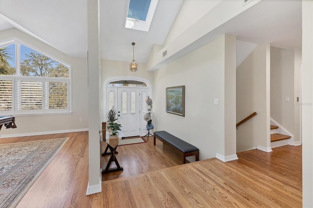 foyer entrance with vaulted ceiling with skylight, visible vents, light wood-style flooring, and baseboards