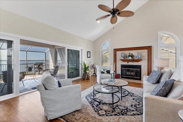 living area with high vaulted ceiling, a tile fireplace, ceiling fan, and wood finished floors