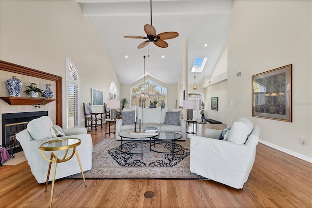 living room with a skylight, wood finished floors, baseboards, beam ceiling, and a glass covered fireplace