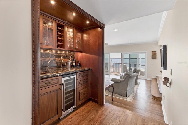 bar featuring light wood finished floors, decorative backsplash, a bar, beverage cooler, and baseboards