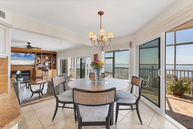 dining room with ceiling fan with notable chandelier, a water view, a fireplace, and light tile patterned floors