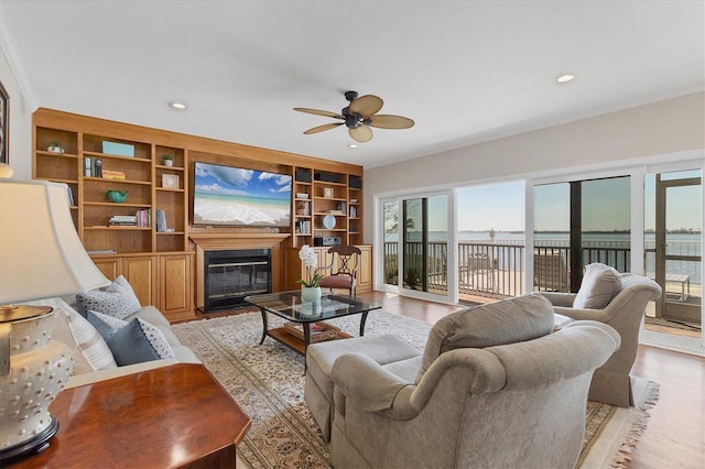 living area featuring light wood-type flooring, recessed lighting, a ceiling fan, and a glass covered fireplace