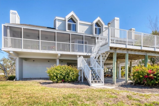 rear view of property featuring a sunroom, a lawn, a chimney, and stairs