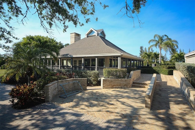 rear view of property with roof with shingles, a chimney, and a sunroom