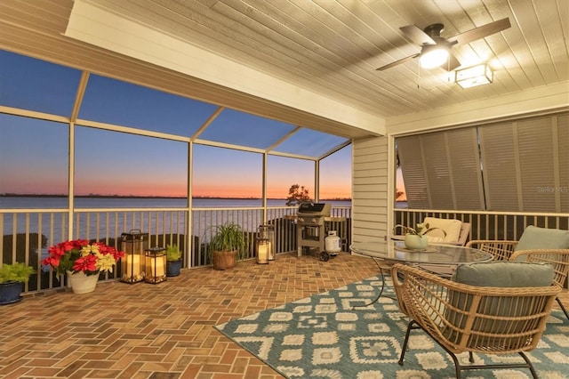 patio terrace at dusk with ceiling fan, glass enclosure, and a water view