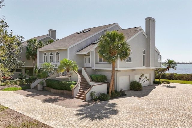 view of front of property with decorative driveway, a chimney, a water view, stairway, and an attached garage