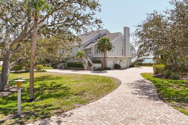 view of front of house with a garage, stairway, decorative driveway, a chimney, and a front yard