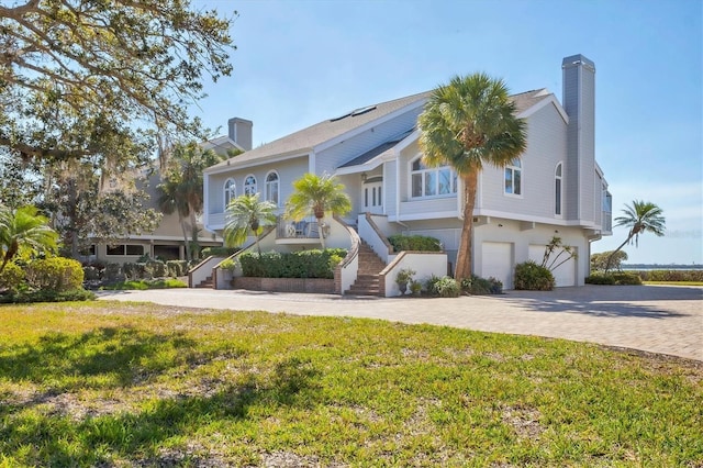 view of front of home featuring decorative driveway, a chimney, an attached garage, a front yard, and stairs