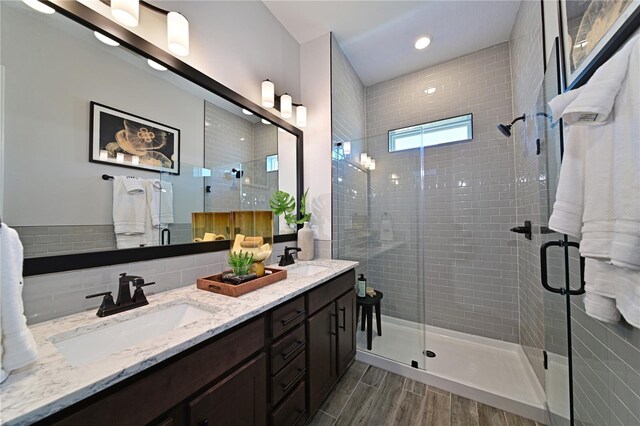 full bath featuring double vanity, wood finish floors, a sink, and a stall shower