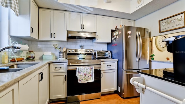 kitchen with a sink, decorative backsplash, stainless steel appliances, white cabinets, and under cabinet range hood