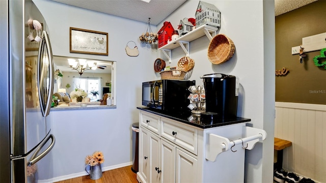 kitchen featuring wainscoting, white cabinets, a textured ceiling, and freestanding refrigerator