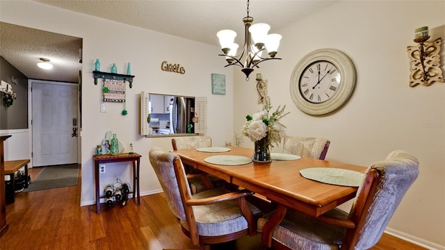 dining space with a notable chandelier, baseboards, a textured ceiling, and wood finished floors