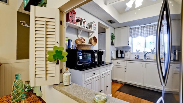 kitchen with visible vents, wood finished floors, stainless steel refrigerator, white cabinets, and a sink