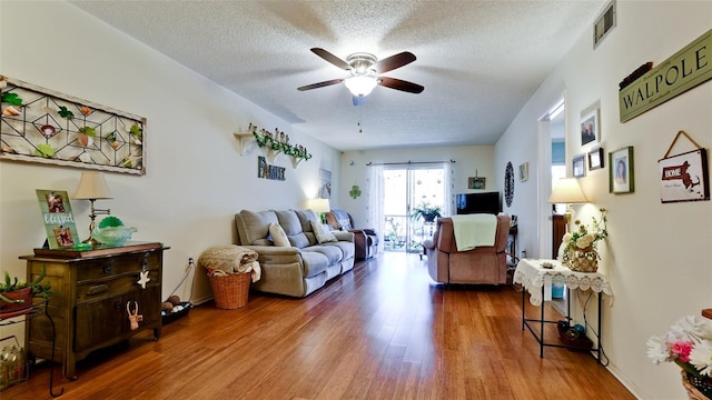 living room with visible vents, a textured ceiling, a ceiling fan, and wood finished floors