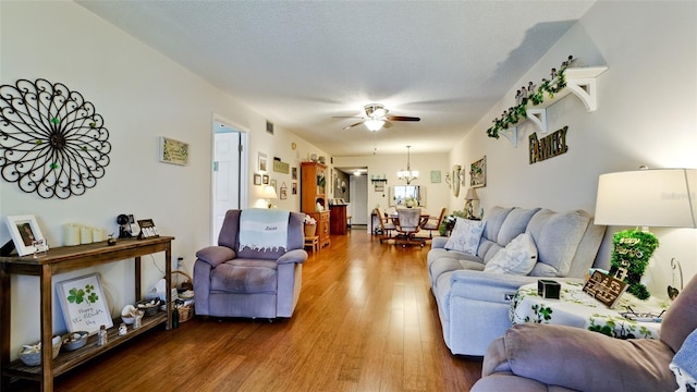 living area with visible vents, ceiling fan with notable chandelier, a textured ceiling, and wood finished floors