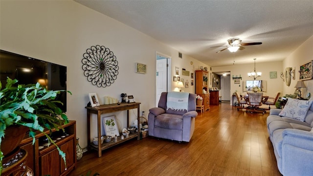 living area with ceiling fan with notable chandelier, dark wood-type flooring, and a textured ceiling