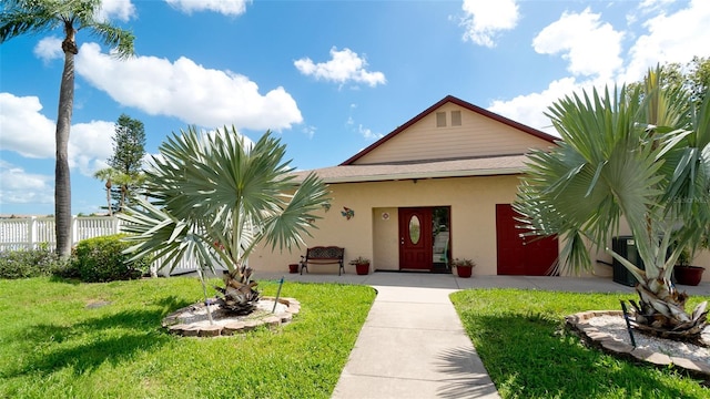 view of front of property with stucco siding, roof with shingles, a front yard, and fence