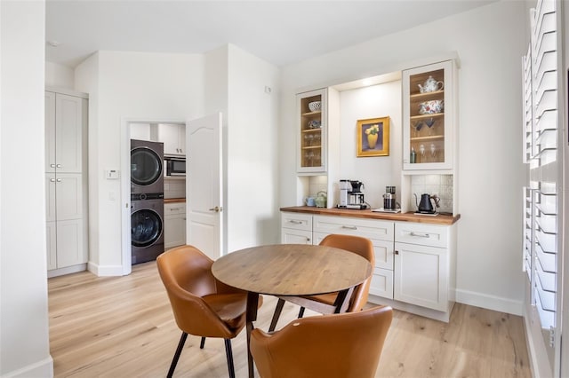 dining room featuring light wood-type flooring, baseboards, and stacked washing maching and dryer