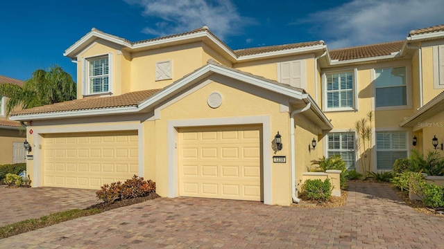 mediterranean / spanish house with a garage, driveway, a tiled roof, and stucco siding