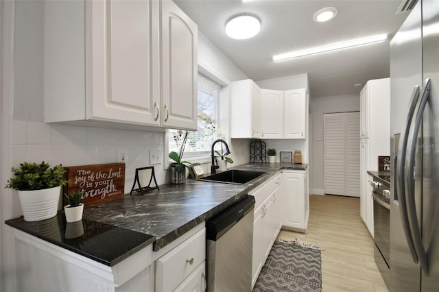 kitchen featuring dark countertops, stainless steel appliances, light wood-style floors, white cabinetry, and a sink