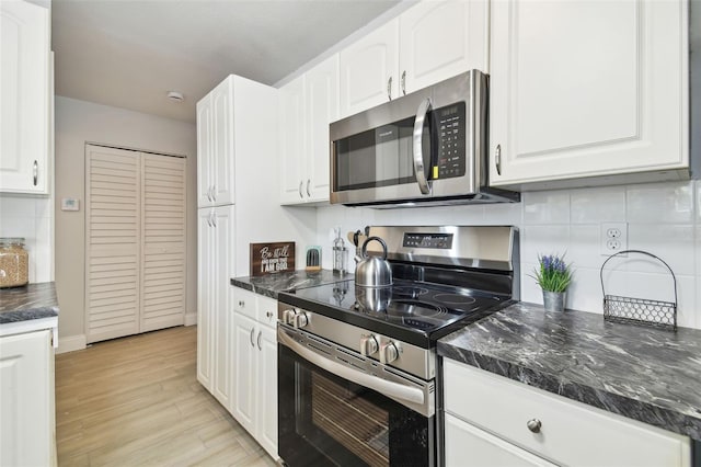 kitchen with light wood-style flooring, white cabinets, appliances with stainless steel finishes, decorative backsplash, and dark stone countertops