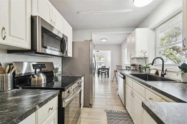 kitchen featuring tasteful backsplash, dark countertops, appliances with stainless steel finishes, white cabinets, and a sink