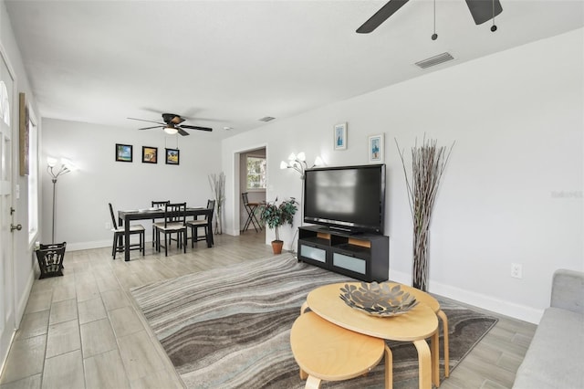 living area with wood finish floors, visible vents, ceiling fan, and baseboards