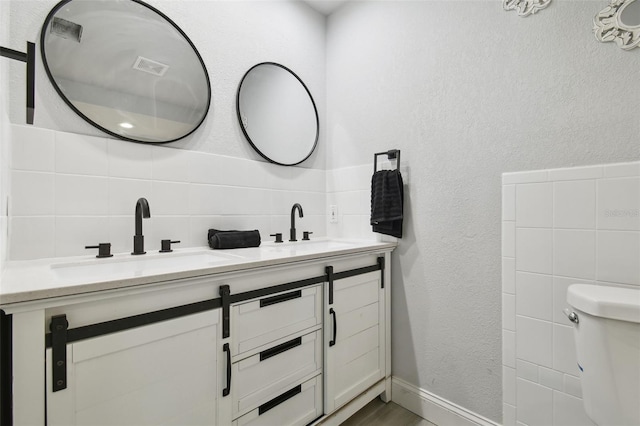 bathroom featuring a textured wall, double vanity, a sink, and toilet