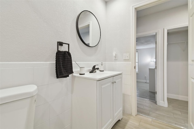 half bathroom featuring wainscoting, toilet, wood tiled floor, vanity, and tile walls