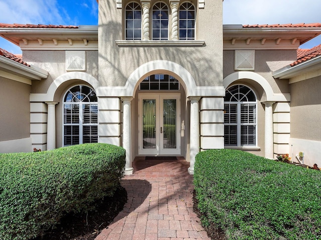 entrance to property with stucco siding, a tiled roof, and french doors