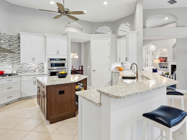 kitchen with a breakfast bar area, light tile patterned flooring, a sink, white cabinetry, and appliances with stainless steel finishes