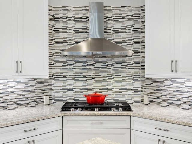 kitchen with wall chimney exhaust hood, decorative backsplash, white cabinetry, and stainless steel gas stovetop