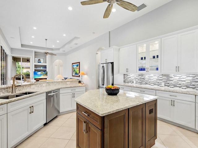 kitchen with light tile patterned floors, arched walkways, a raised ceiling, appliances with stainless steel finishes, and a sink