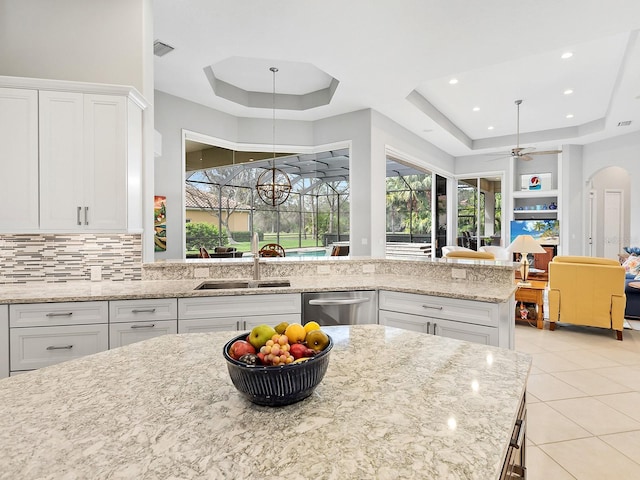 kitchen featuring arched walkways, a raised ceiling, white cabinetry, a sink, and dishwasher