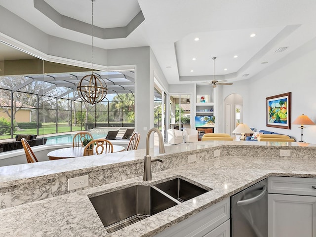 kitchen with light stone counters, a sink, white cabinetry, open floor plan, and a raised ceiling