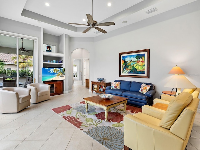 living area featuring light tile patterned floors, visible vents, arched walkways, a raised ceiling, and recessed lighting