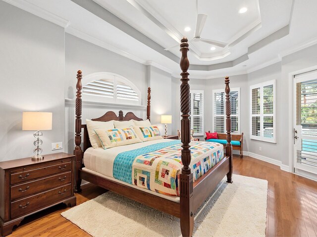 bedroom featuring baseboards, wood finished floors, a tray ceiling, crown molding, and recessed lighting